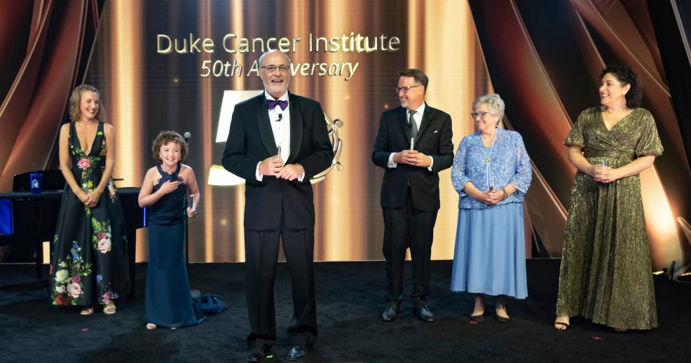 Michael Kaston on a stage surrounded by cancer survivors and their family members in front of DCI 50th anniversary logo