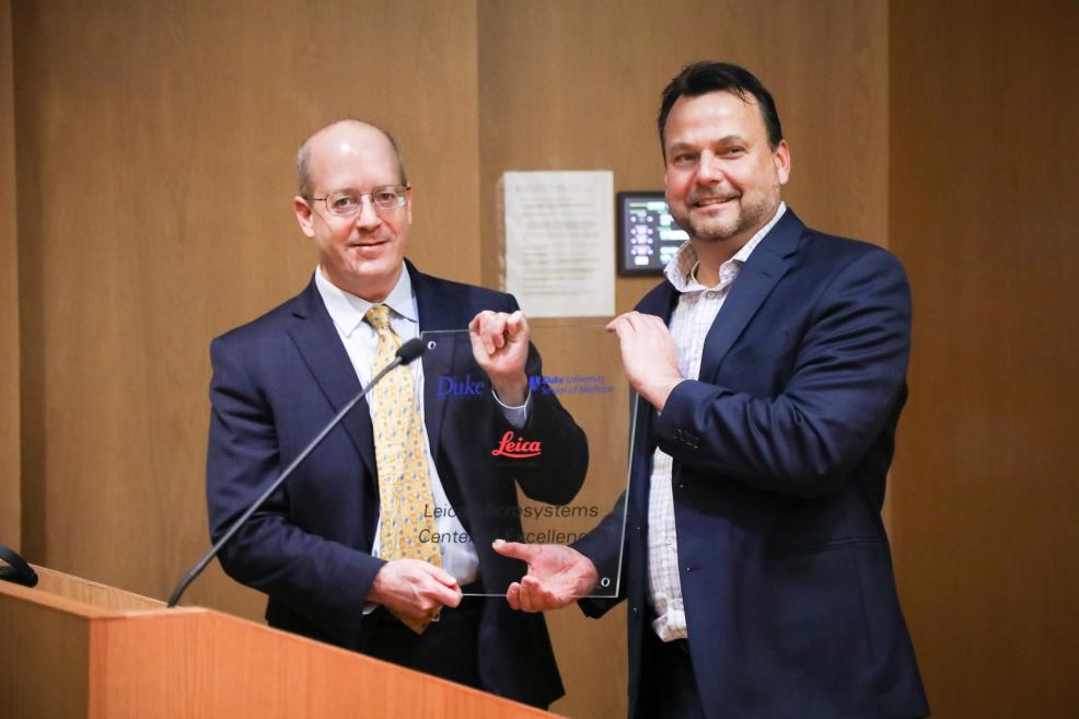 Lawrence Carin, PhD, and Greg Eppink pose with a special glass plaque created for the new Leica Microsystems Center for Excellence 
