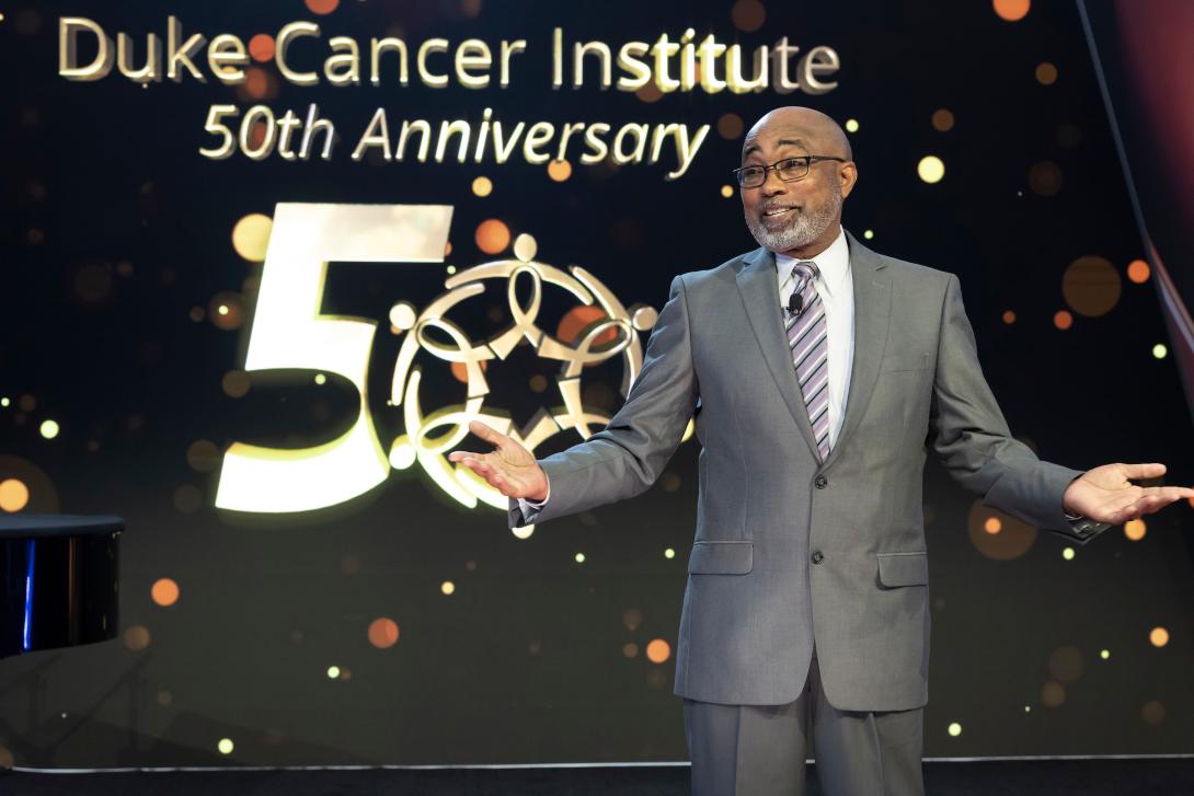 Cancer survivor Ovester Grays on stage with Duke Cancer Institute 50th anniversary logo behind him.