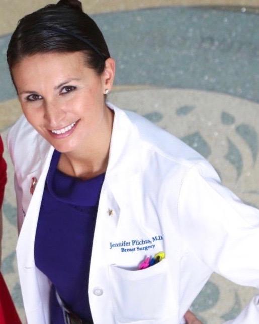 Jennifer Plichta has her hands on her hips and is wearing a white lab coat.