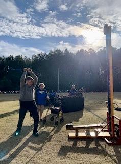 Man swings a sledgehammer next to a strongman game with bell