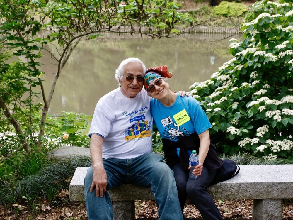 Man and woman sit on a bench in Duke Gardens, smiling