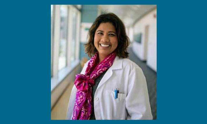 A woman wearing a white lab coat stands in a sunlit hallway