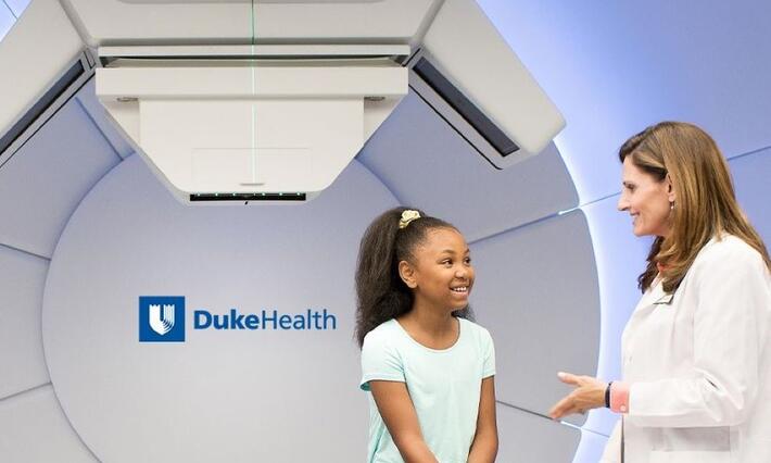 Photo of a doctor and child sitting in front of a proton beam machine