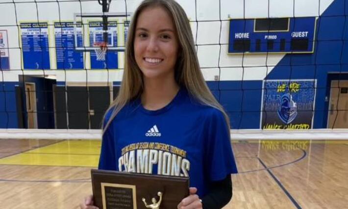 Addison Rowan smiles on the volleyball court holding a plaque