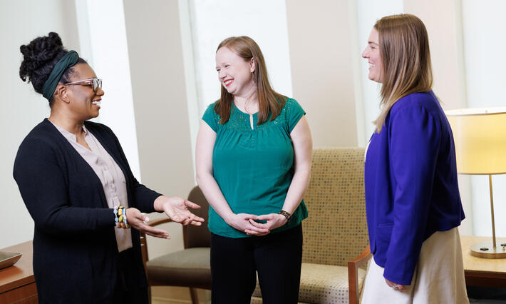 Three women in business casual clothing talking and smiling.