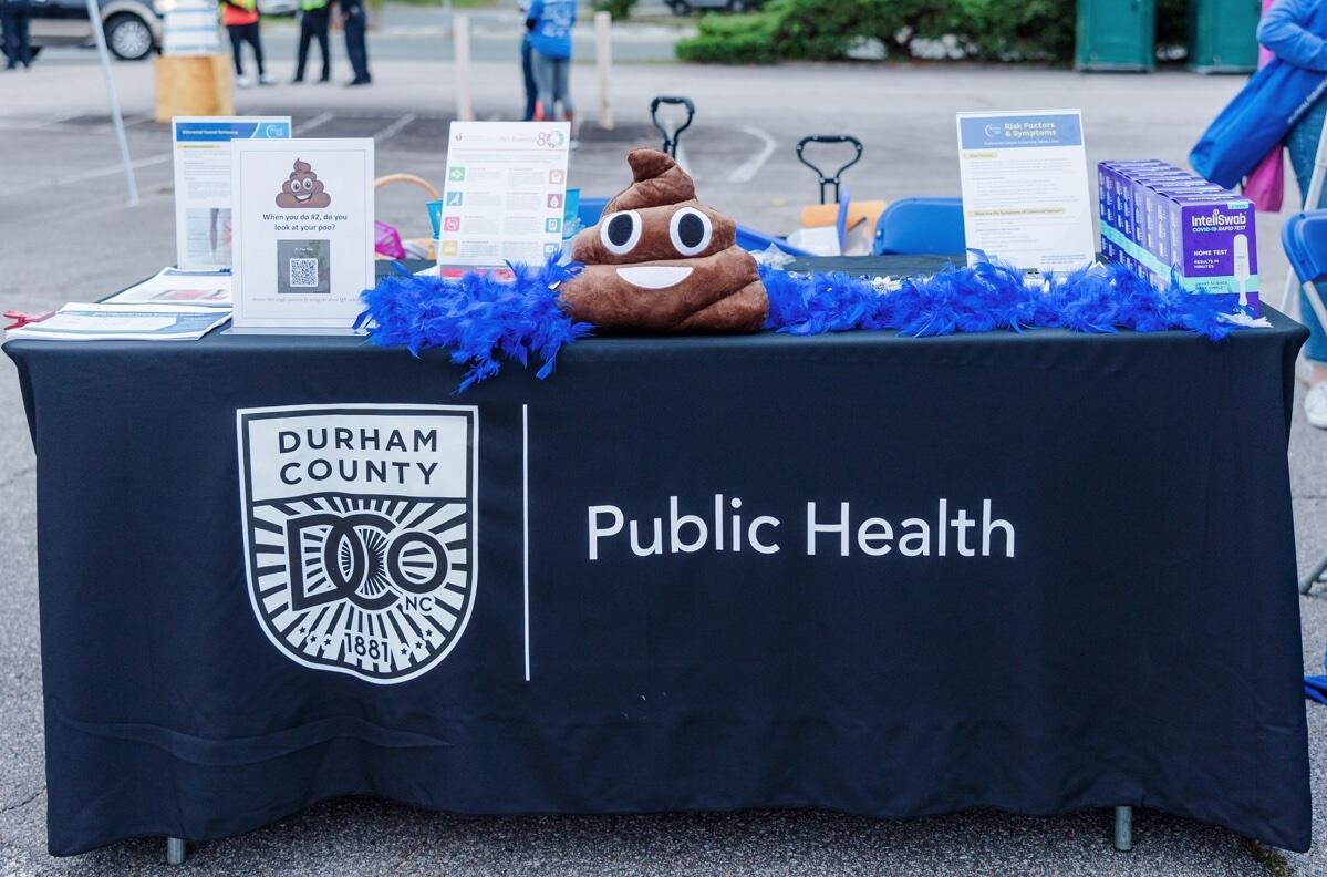 Table draped in black with insignia of Durham County Public Health with sign that says "When you do #2, do you look at your poo" and a poop emoji toy