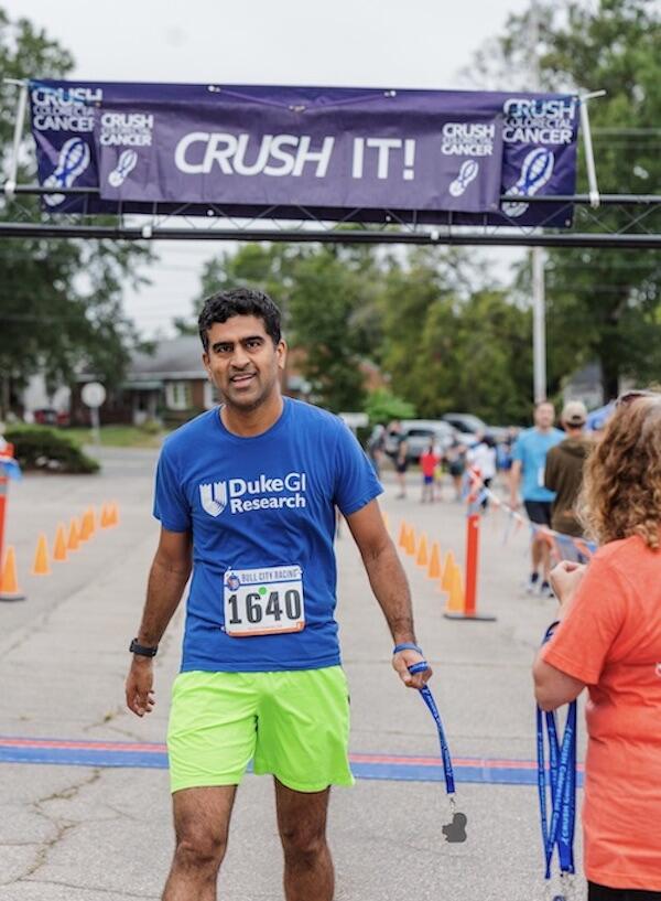 man with CRUSH t-shirt under the CRUSH sign holding a ribbon with a medal attached to it