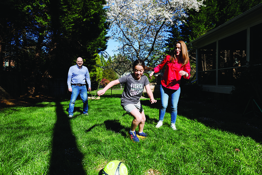 A family of three runs in a grassy yard.