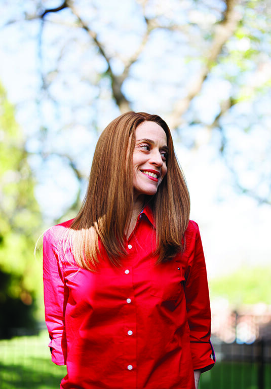 A woman in a red blouse smiles and looks into the distance.