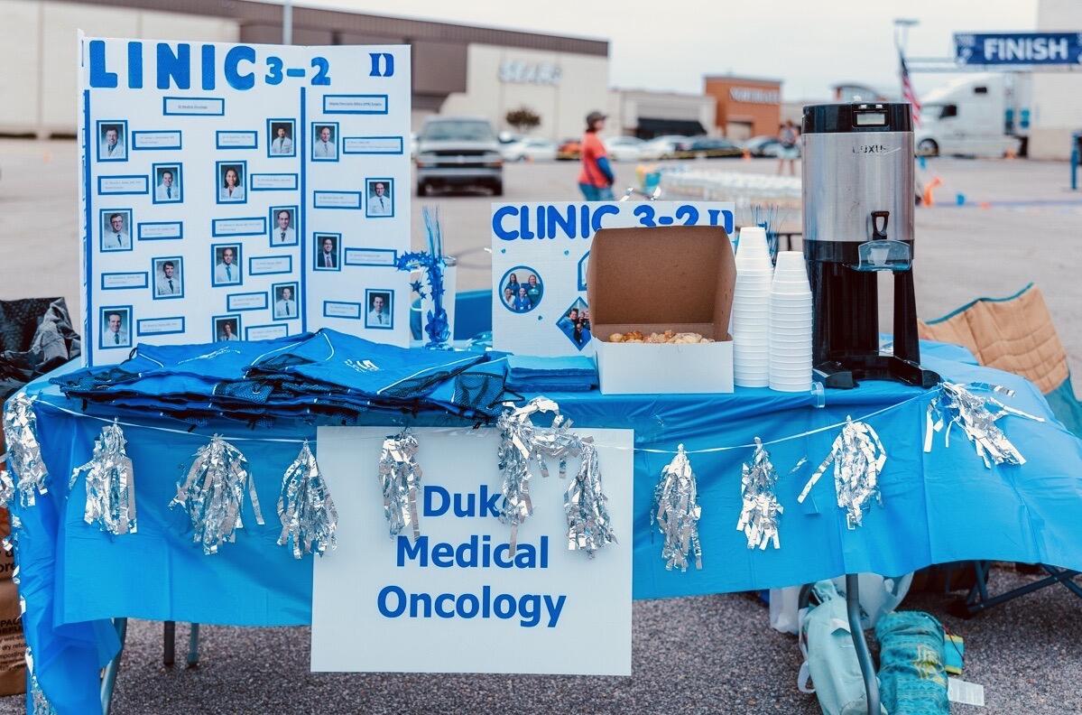 a table draped in blue with signs that read Clinic 3-2 and Duke Medical Oncology and posterboard with photos of clinicians