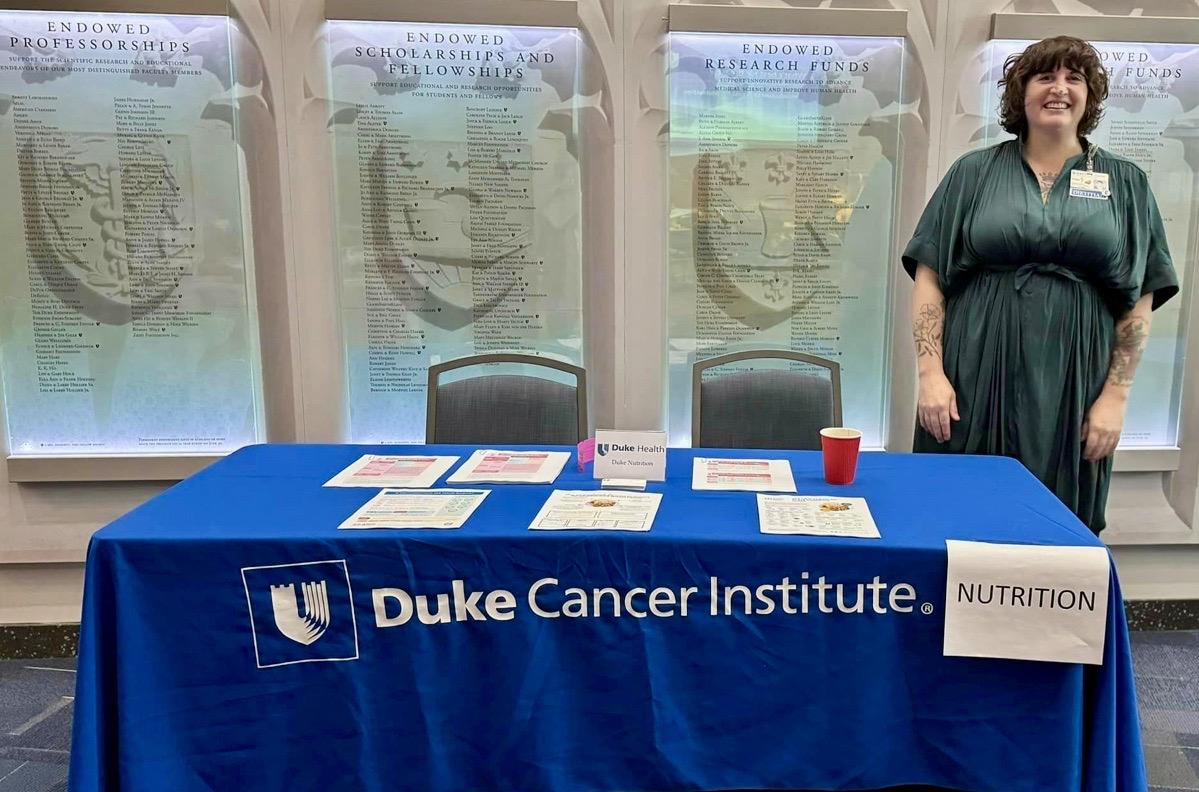 a woman standing behind a table draped in a blue cloth labeled Duke Cancer Institute and with a "nutrition" sign