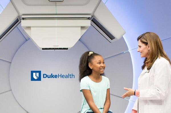 Photo of a doctor and child sitting in front of a proton beam machine