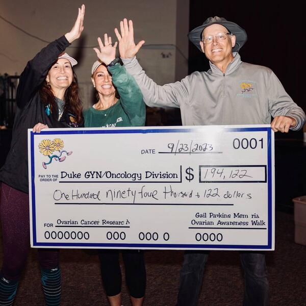 Three people hold up a donation check and smile