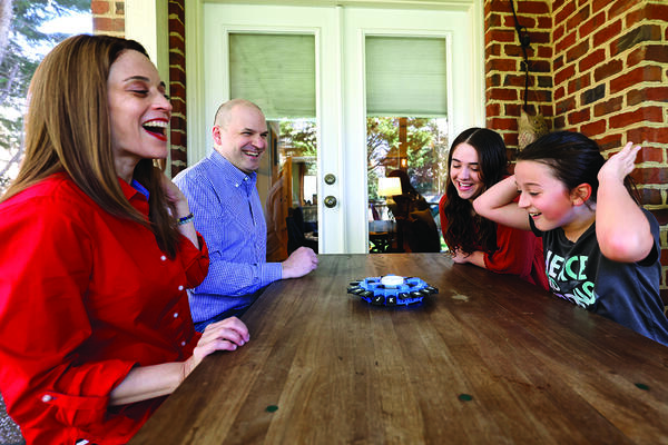 Bottom a family of four smiles and laughs at an outdoor table playing a game.