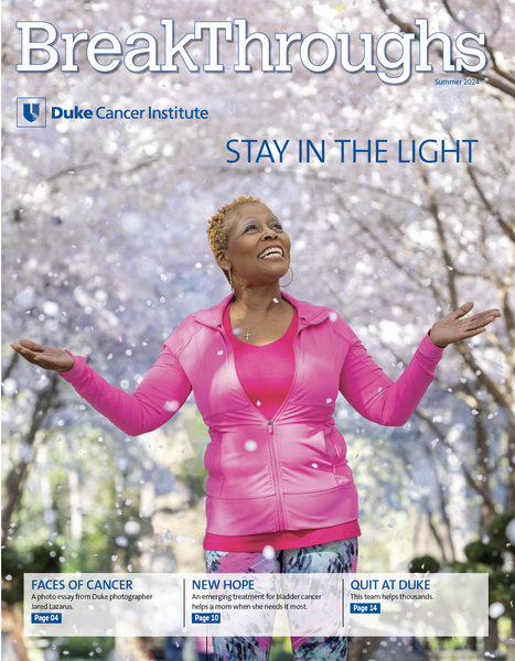 A woman in a pink jogging suit with her hands outstretched in front of cherry trees.