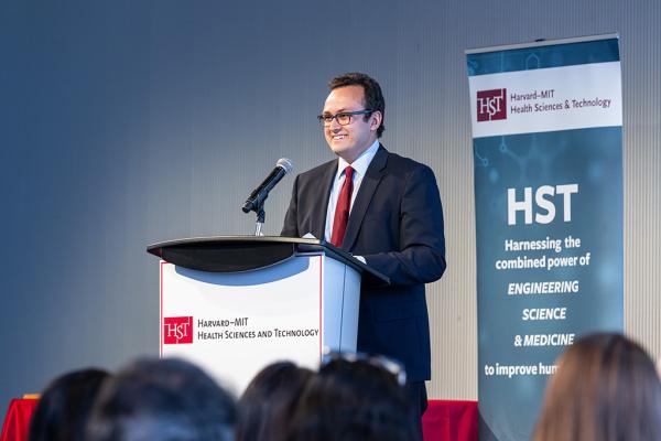 Kameron Kooshesh, MD, at a lectern in front of a Harvard Health Sciences sign
