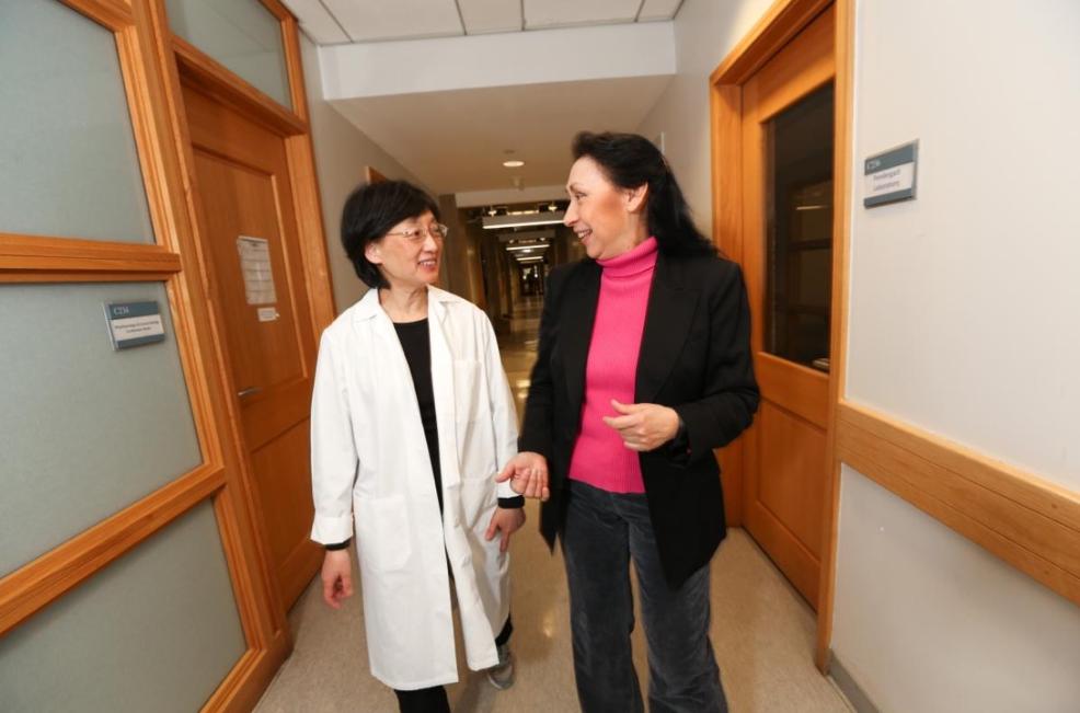 two women, one in a labcoat, walk and talk in a hallway