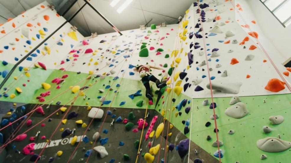 indoor tall climbing wall with multi-colored fake rocks jutting out and person climbing