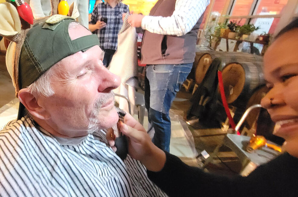 man in backwards baseball cap gets his mustache shaved by woman holding razor to his face