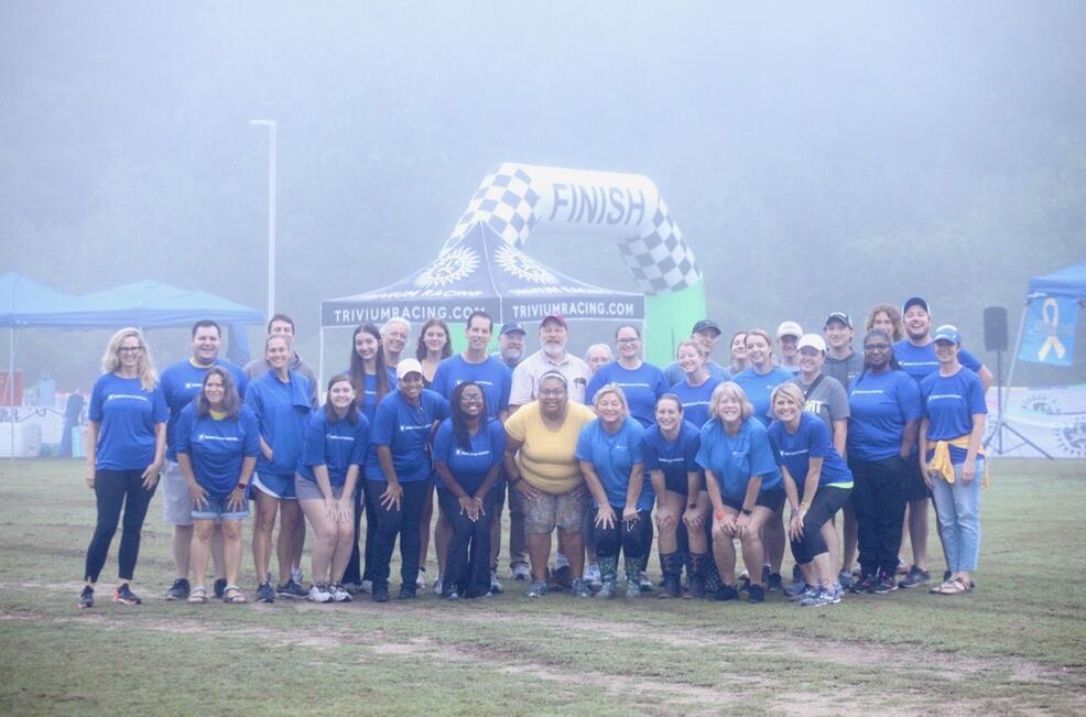 About two dozen Team DCI members clad in blue shirts gather on a misty field