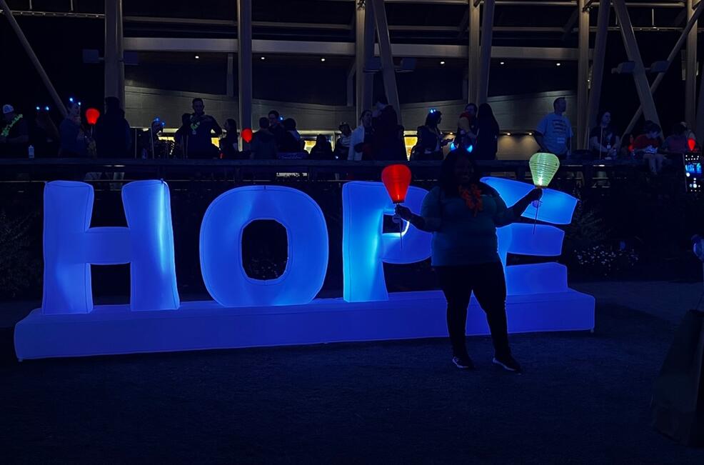 a blue inflated "Hope" sign is illuminated. A woman holds a red and a white lantern.