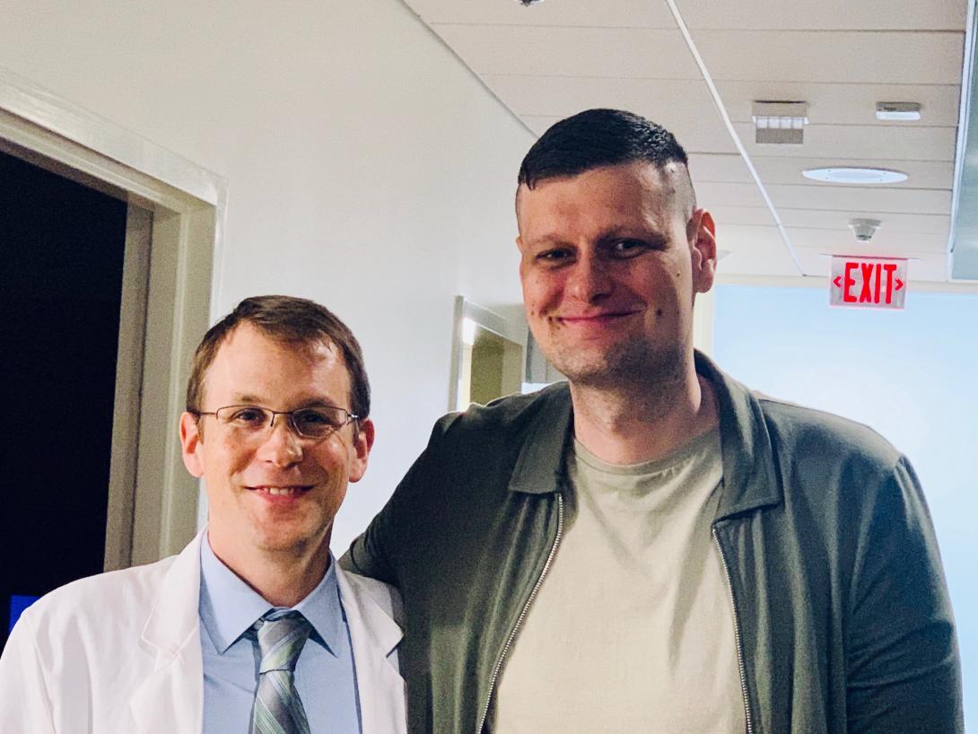 Dr. John Strickler stands next to Milos Bogetic in the DCI clinic hallway. Milos towers above.