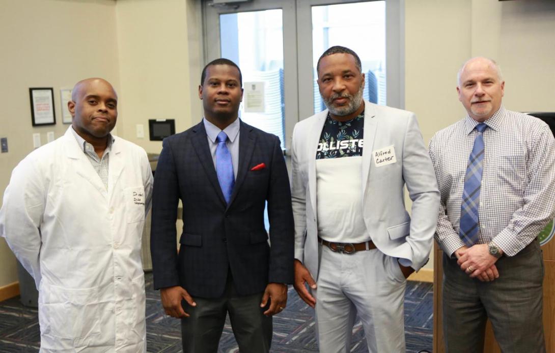 Four men posing, one in a lab coat, two in suit jackets, one in a shirt and tie