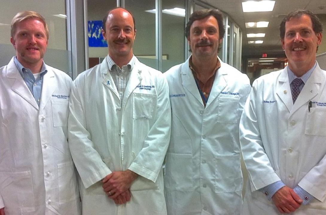 Four men in white lab coats stand together 