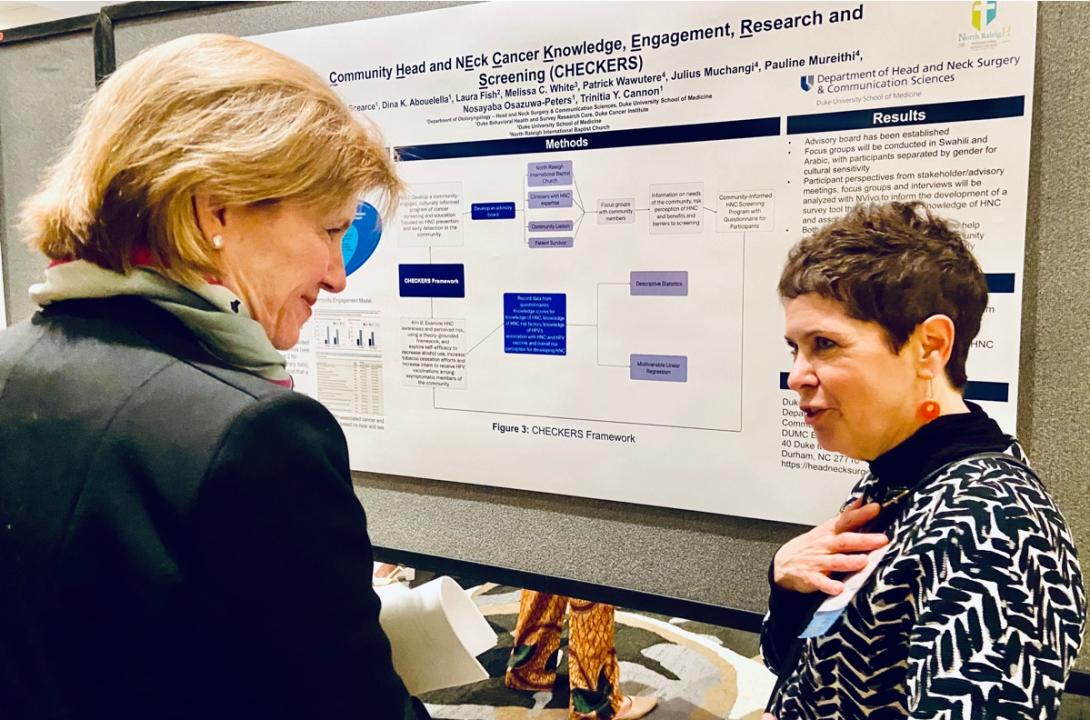 Dean Mary Klotman and Leda Scearce talk in front of a poster presentation on "Community Head and Neck Cancer Knowledge, Engagement, Research and Screening (CHECKERS)"