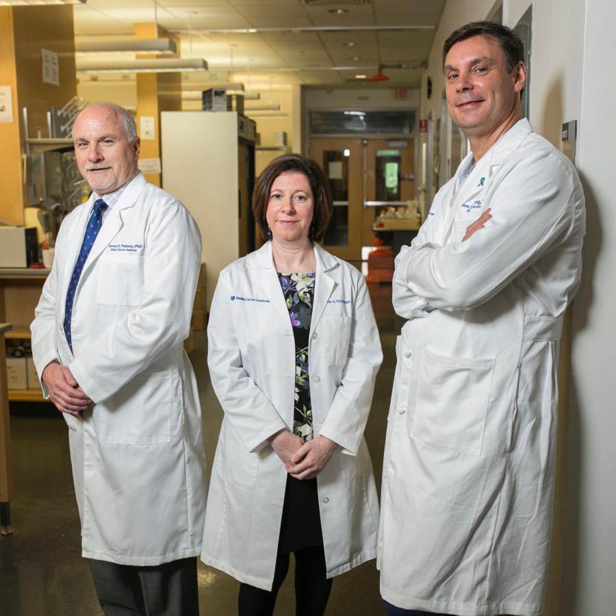 Two men and a woman in lab coats pose in the lab